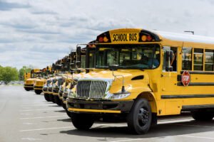 long line of yellow school buses parked in a row out front of high school
